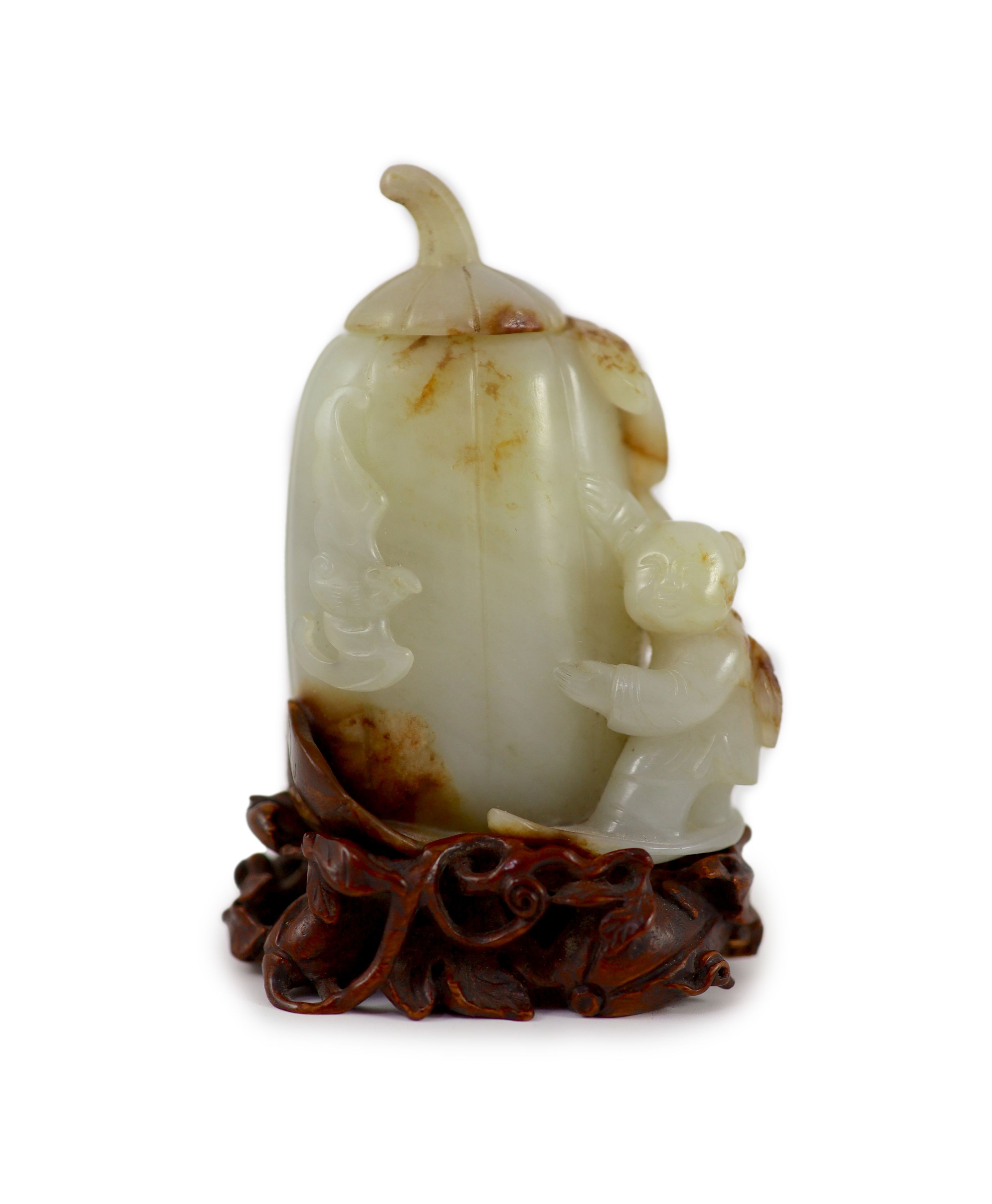 A Chinese pale celadon and russet jade 'boy' jar and cover, 8.3 cm high, the hardwood stand carved as a vine